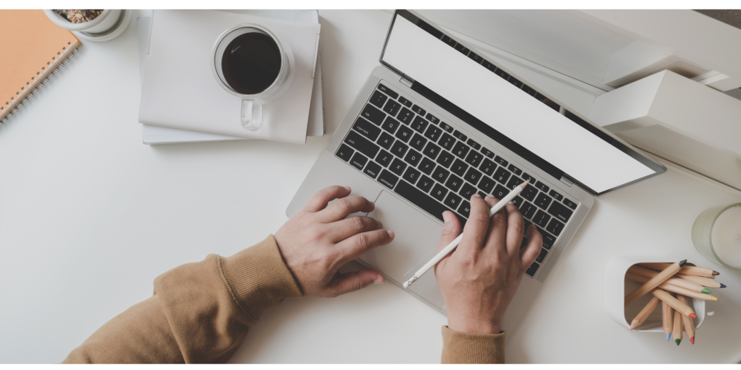 Pessoa digitando em um Notebook com uma caneta na mão diretia trabalhando com Marketing Digital